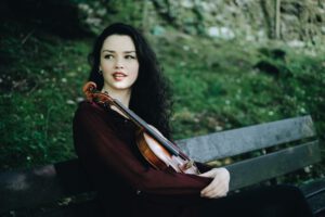 Mairéad Hickey with Violin under her chin sitting on a bench